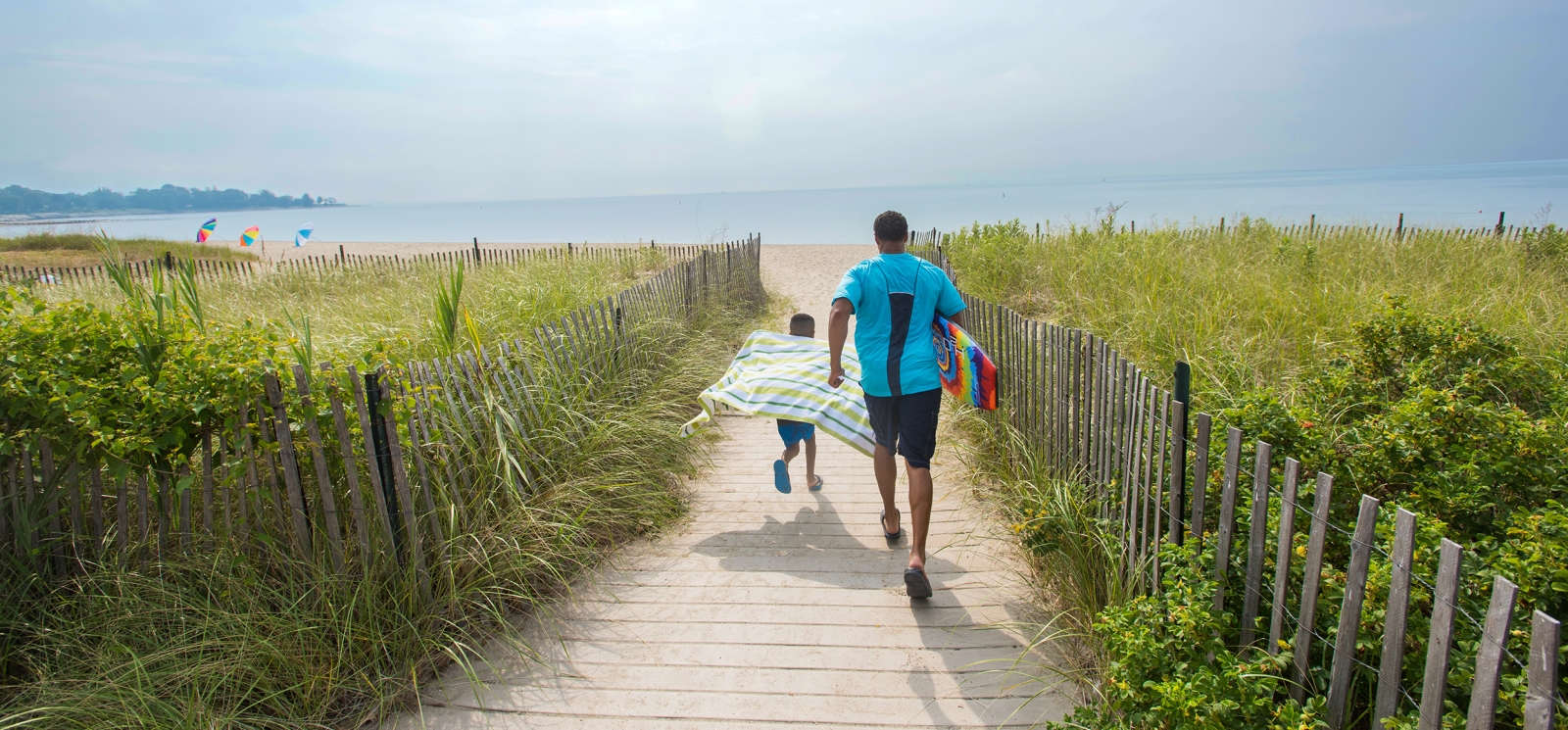 Father and son running down path toward beach at Sherwood Island State Park
