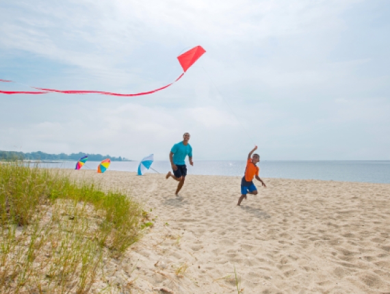 Father and son running toward water flying a kite on Sherwood Island